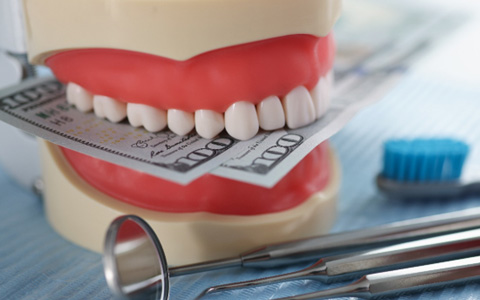 A jaw mockup biting down on hundred-dollar bills