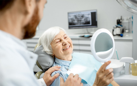 Older woman looking at her smile at the dentist’s office