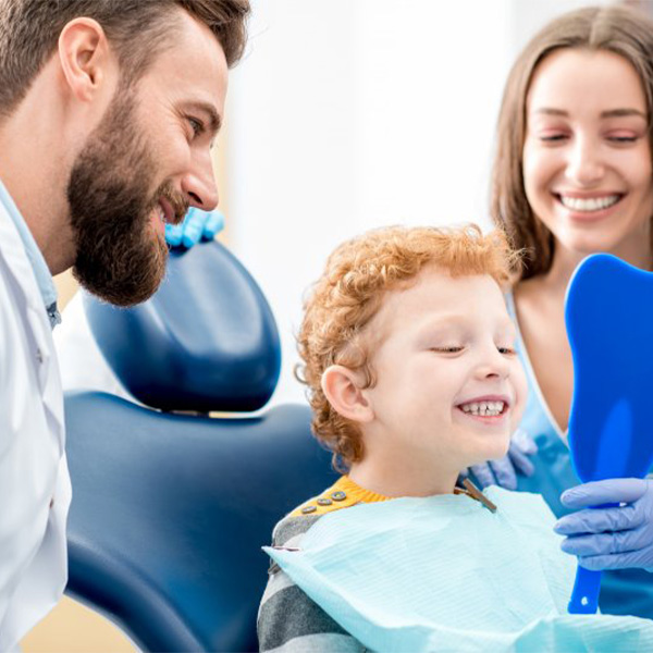 Child smiling in a small mirror after a dental cleaning.